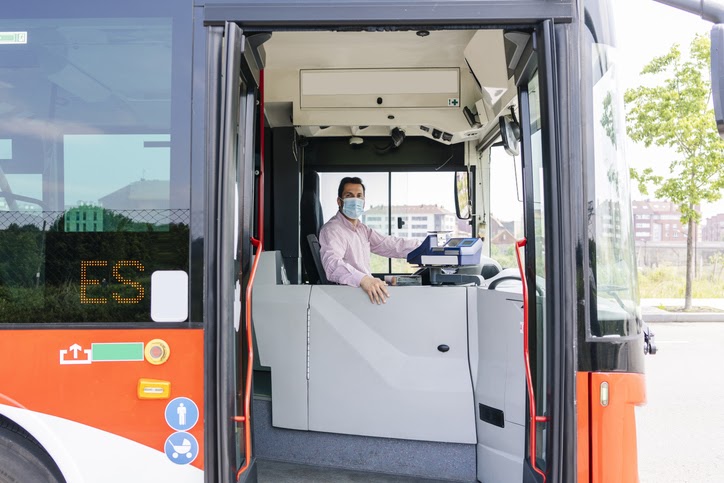 Bus driver wearing protective mask waiting at bus station, Spain.