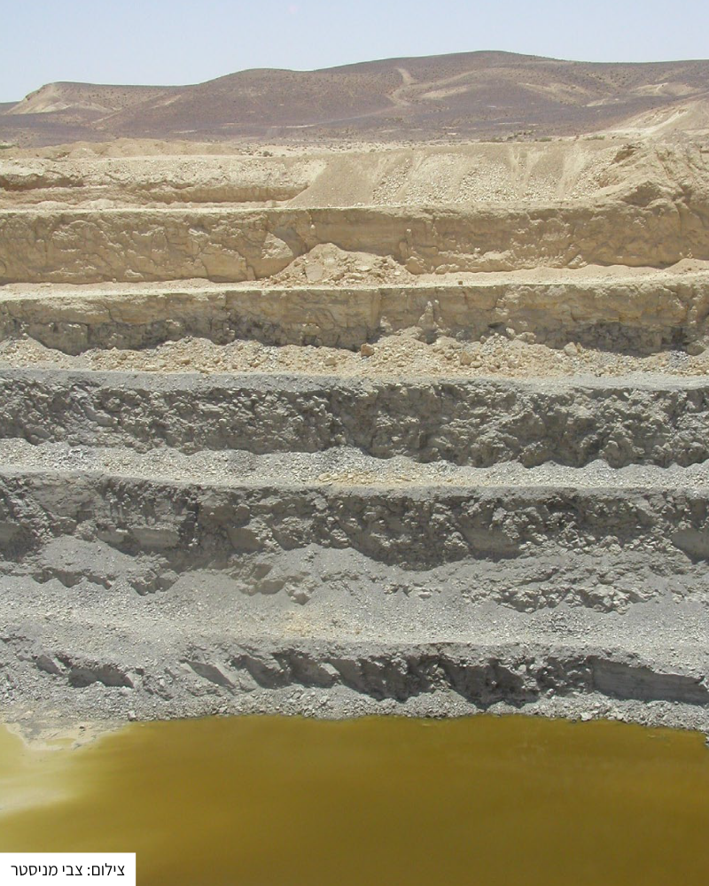 שכבות שונות של קרקע בצבע בז׳ ואפור עם שלולית מים בצבע חרדל במכרה פצלי שמן.