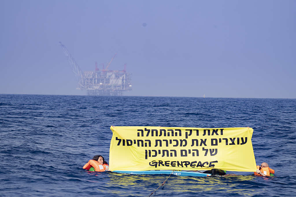 שני פעילי גרינפיס מחזיקים שלט מחאה נגד קידוחי דלקים בים התיכון כשהם בתוך הים על רקע אסדת הגז לוויתן.