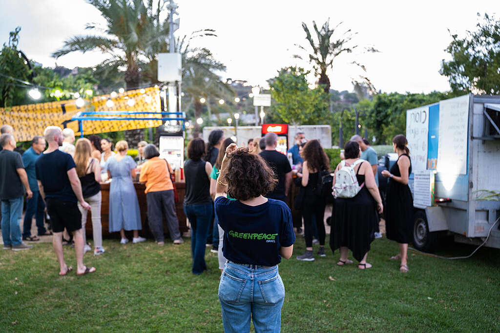 אישה עם חולצה של גרינפיס עומדת ומסתכלת על עמדת מכירת בירה בכוסות רב-פעמיות.