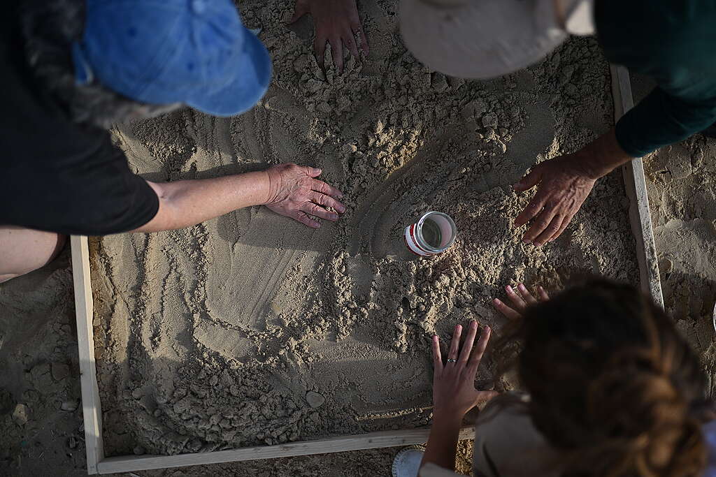 שלושה אנשים רוכנים על חול ים עם צנצנת באמצע לאיסוף נורדלים.