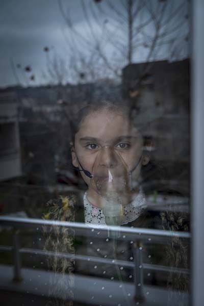 ילדה מסתכלת דרך החלון עם מסכת חמצן על הפנים