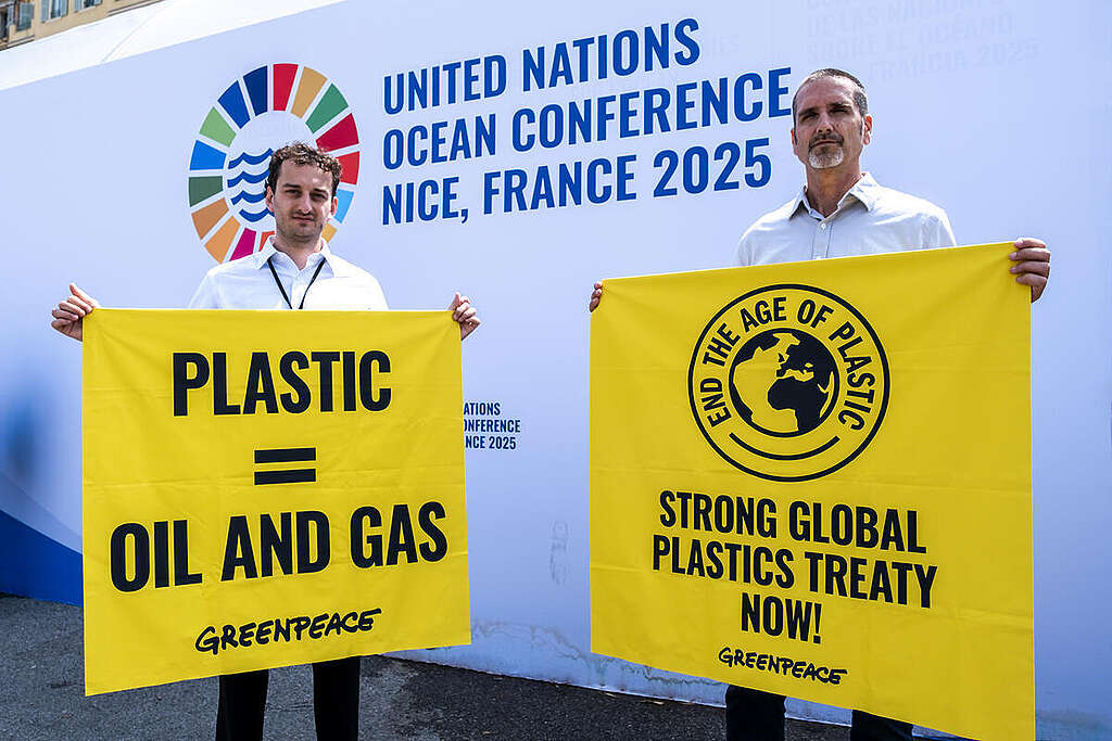 שני גברים פעילי גרינפיס מחזיקים שלטים צהובים נגד תעשיית הפלסטיק בוועידת האוקיינוסים של האו״ם.