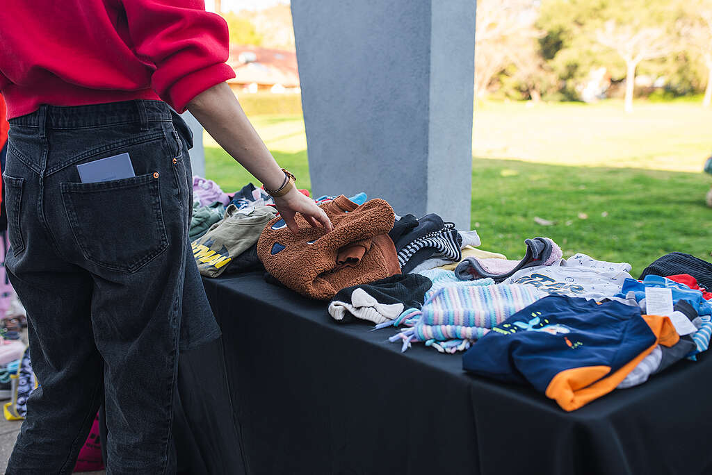 אישה עומדת ליד שולחן עם בגדי ילדים יד שנייה.