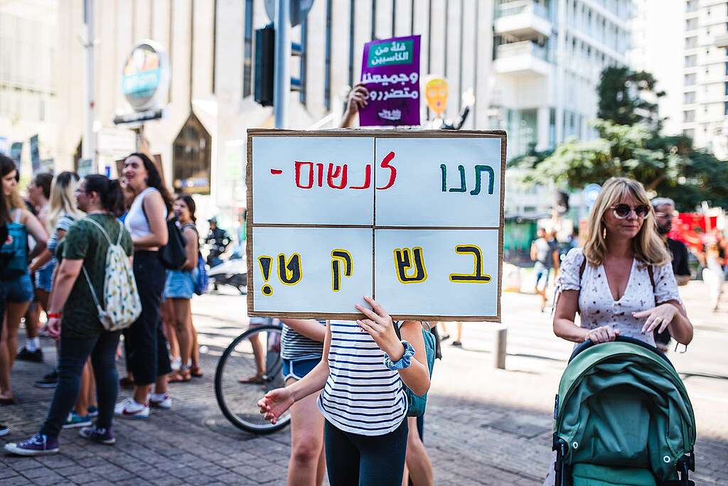 ילדה מחזיקה שלט ברחוב בתל אביב שכתוב עליו ״תנו לנשום בשקט״