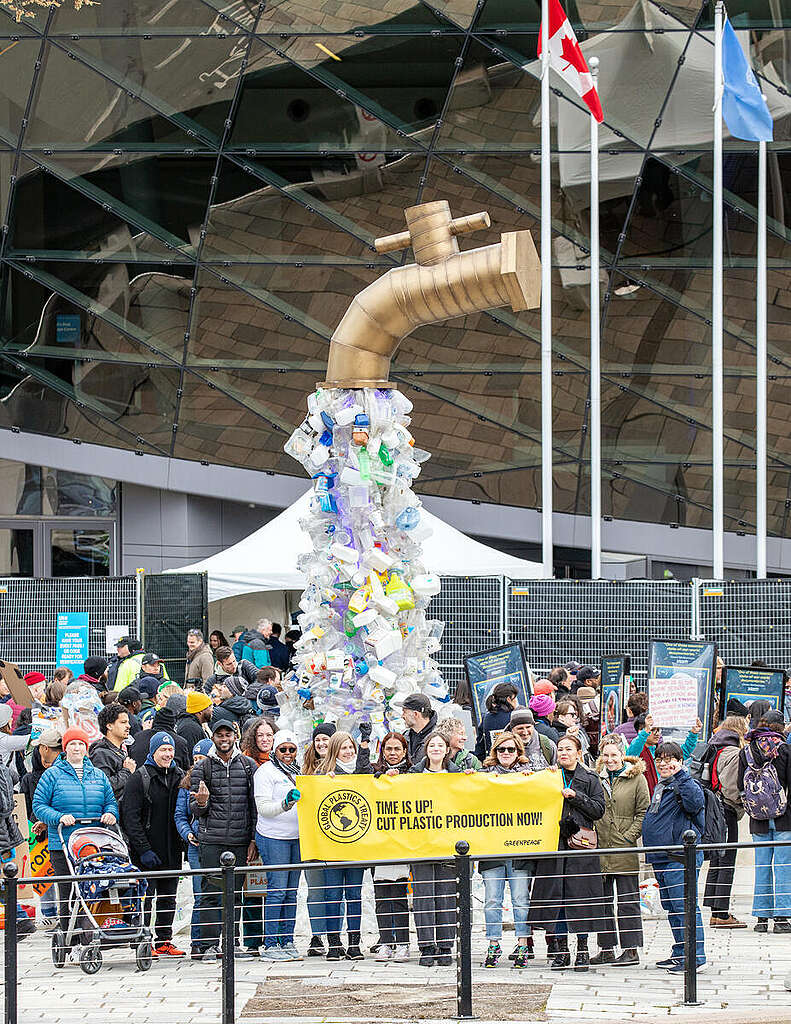 מיצב של ברז ממנו נשפכת פסולת פלסטיק ולידו קבוצה של פעילי גרינפיס מחזיקים שלט צהוב עליו כתוב ״הזמן אזל! חתכו את ייצור הפלסטיק עכשיו!״