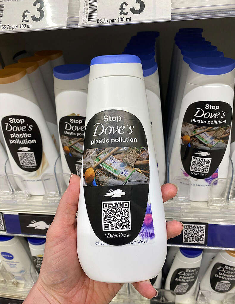 פעיל גרינפיס מראה בקבוק שמפו של חברת ״דאב״ עם מדבקה אלטרנטיבית שגרינפיס הכין עליה כתוב ״עצרו את זיהום הפלסטיק של דאב״.