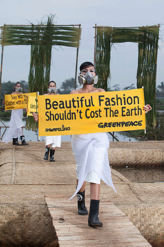 תצוגת אופנה כשהדוגמניות עם מסיכות סינון אוויר ומחזיקות שלטים נגד הזיהום של תעשיית האופנה.