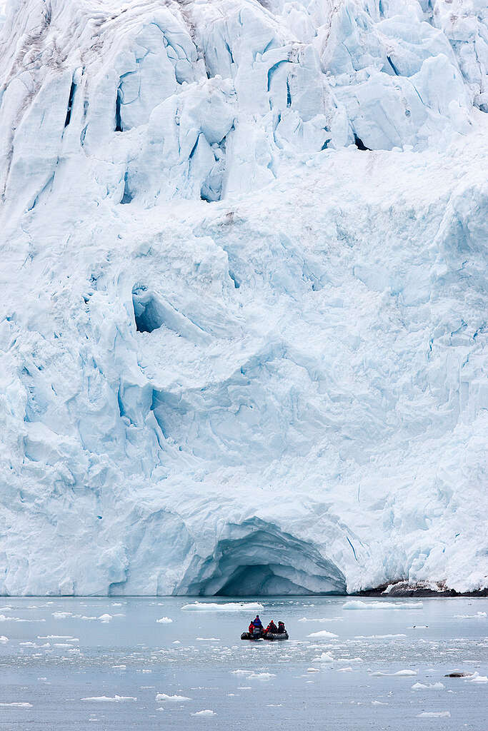 קרחון עצום ומתחתיו בים סירה מתנפחת קטנה
