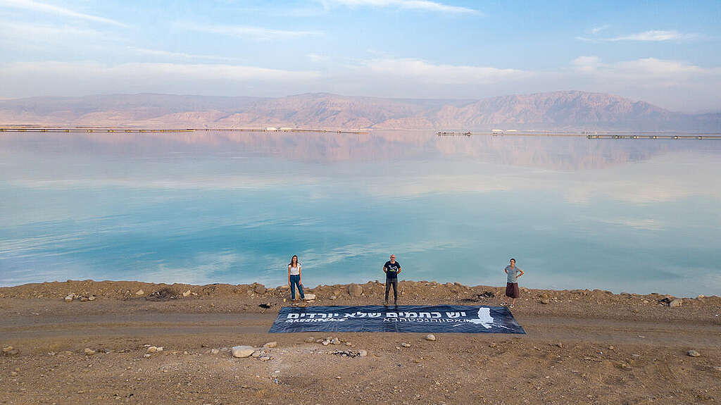 שלושה פעילים של גרינפיס עם באנר גדול פרוס על האדמה ועליו כתוב ״יש כתמים שלא יורדים״ על רקע ים המלח.