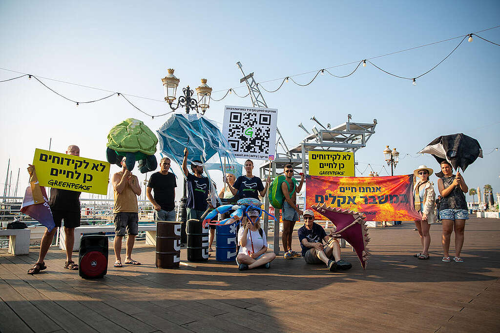 פעילי גרינפיס עומדים בטיילת עם שלטים שונים ובובות גדולות של בעלי חיים ימיים.