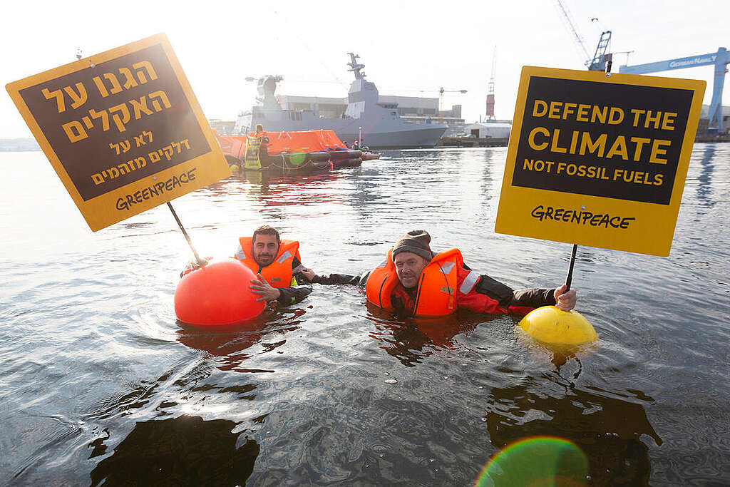 שני פעילי גרינפיס עם חליפות הצלה כתומות צפים בים ומחזיקים שלטים צהובים עליהם כתוב ״הגנו על האקלים, לא על דלקים מזהמים״