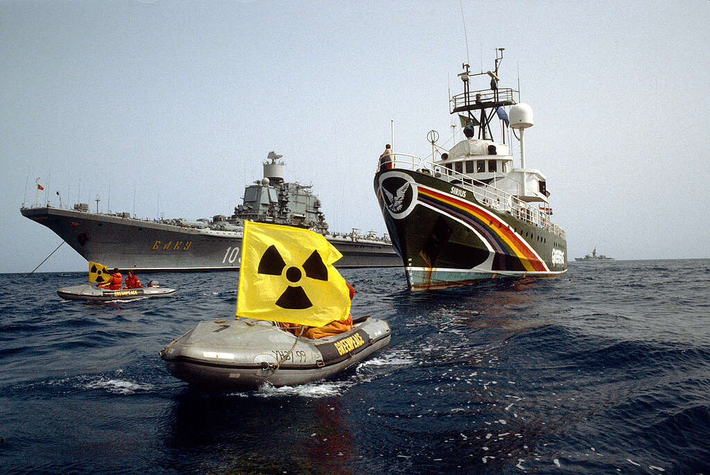 שתי סירות מתנפחות של גרינפיס בים עם דגלים צהובים נגד אנרגיה גרעינית, שטות מול ספינה גדולה לצד ספינת גרינפיס