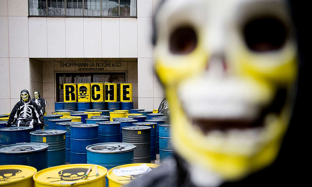 חביות כחולות וצהובות עם גולגלות מצוירות בחלקן העליון וביניהן פעילי גרינפיס עם תלבושת ומסיכת שלד.