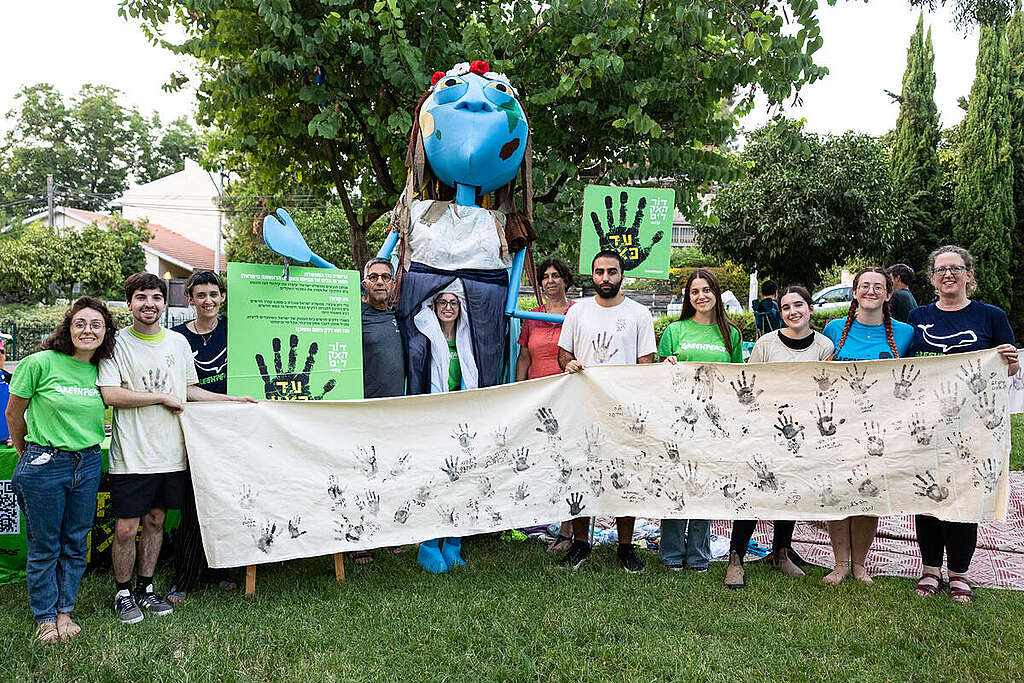 פעילי גרינפיס עומדים בשורה עם בד לבן ועליו טביעות יד בדיו שחורה. 