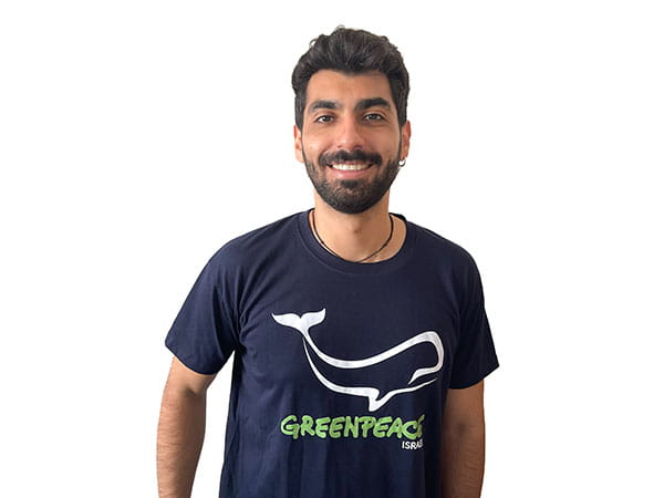 איש צעיר מחייך בחולצת Greenpeace ישראל עם לוגו של לוויתן