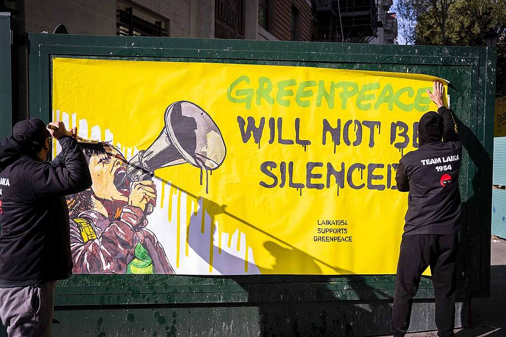 Due attivisti attaccano il manifesto di Laika con la scritta "Greenpeace will not be silenced", ovvero "Greenpeace non sarà messa a tacere"