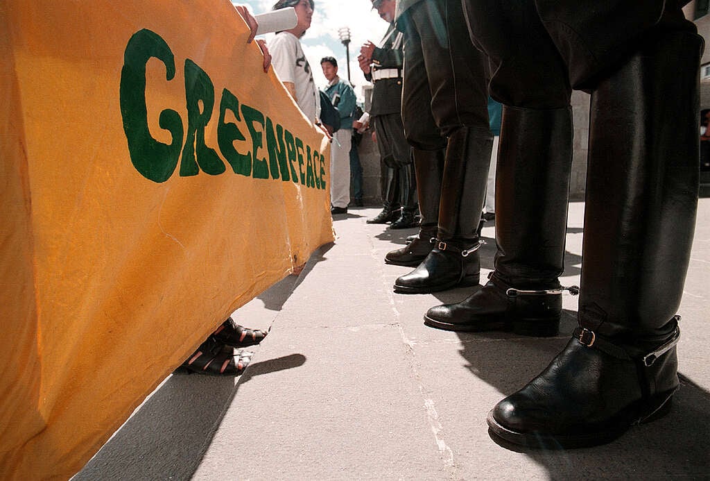 Attivisti reggono uno striscione con il logo di Greenpeace di fronte a un cordone di poliziotti