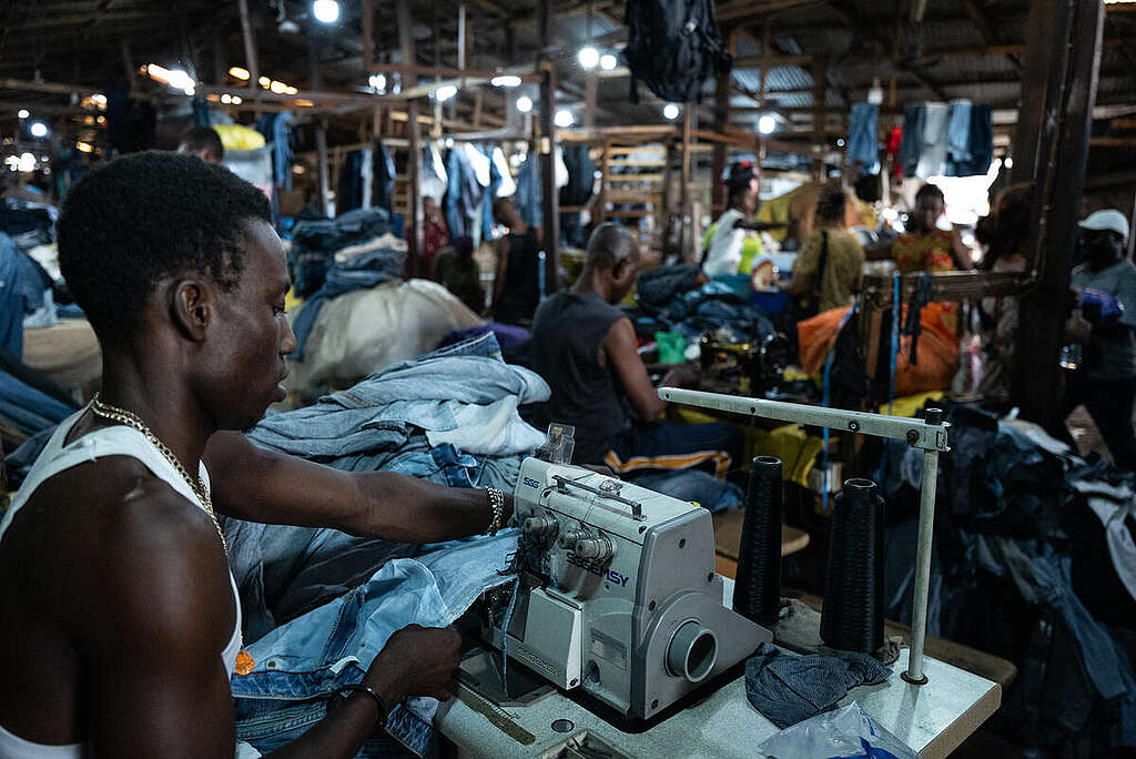 Un uomo ripara dei jeans con la macchina da cucire all'interno del mercato di Kantamanto, in Ghana,