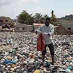 Reporter Mike Anane looks at textile waste at the Weija Ashbread landfill, an older textile dump site sited on the Densu river, upriver from the protected wetlands, outside Accra, Ghana.