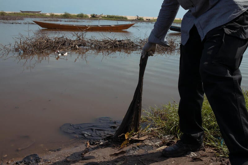 Un uomo sulla riva di un fiume estrae degli abiti rimasti incastrati nella sabbia Un uomo sulla riva di un fiume estrae degli abiti rimasti incastrati nella sabbia