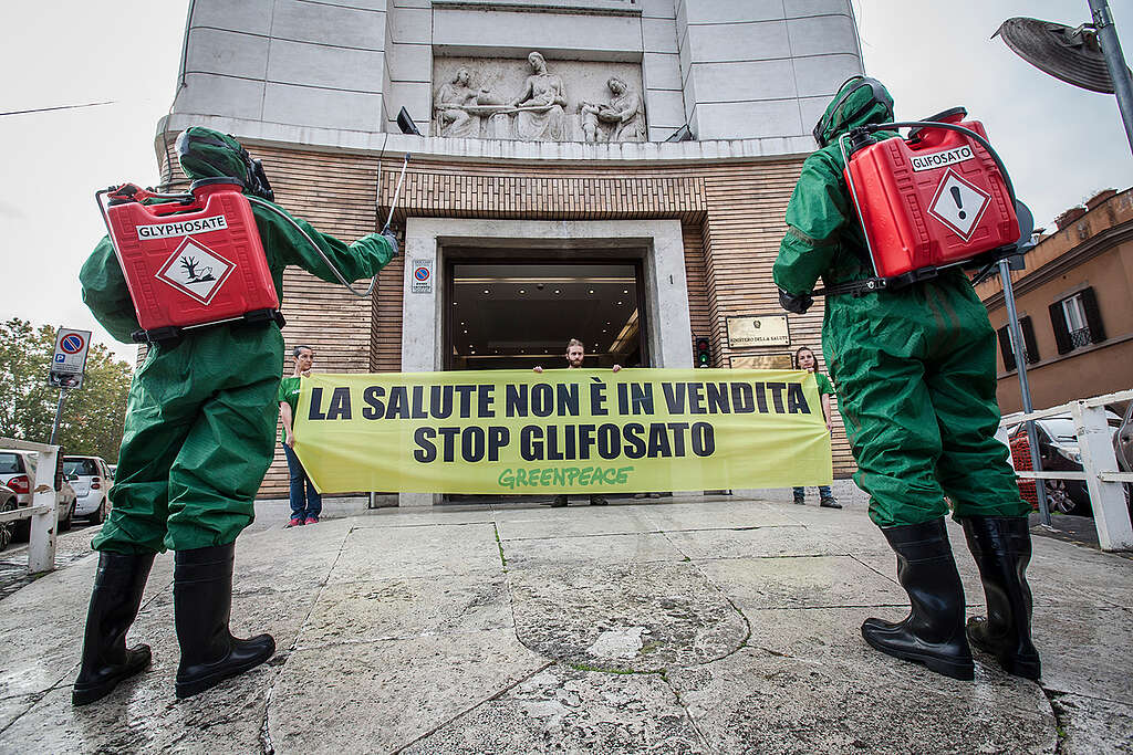 
Attivisti di Greenpeace vestiti con tuta protettiva, maschera antigas ed erogatore di pesticidi a spalla, simulano l’irrorazione con il glifosato davanti al Ministero della Salute