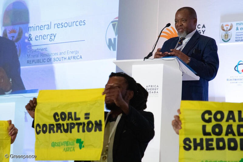 マンタシェ大臣の前で、「石炭＝汚職」と書かれたバナーを掲げるグリーンピース・アフリカのメンバーたち