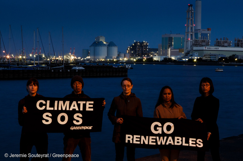 磯子火力発電所と南横浜火力発電所を背に、「気候のSOS」、「再生可能へ」と書かれたバナーを掲げるグリーンピースのスタッフ。