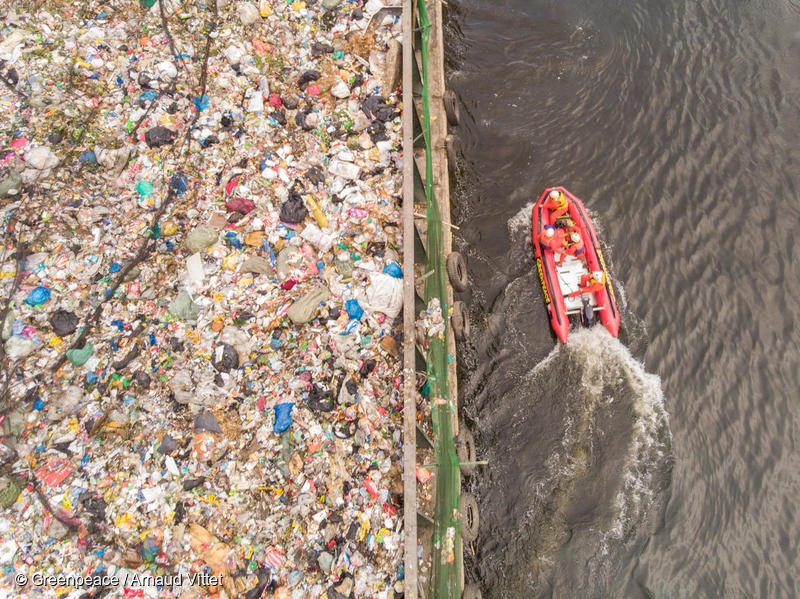 マニラ湾を通過する何トンものプラスチック廃棄物を積んだ運搬船と抗議行動を行うグリーンピースのボート