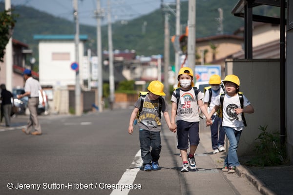 Children walk along a road which had earlier been assessed by a Greenpeace team- led by Jan Beranek - for radioactive contamination, and found to hold high unsafe levels of the contamination, in Fukushima city, in Fukushima prefecture, Japan, on Tuesday 7th June 2011. The city of Fukushima has been contaminated by radioactive fallout from the ongoing crisis at the Fukushima Daiichi nuclear plant. Within Fukushima city the local authorities are now undertaking a clean up of soil from school and nursery school playgrounds.
