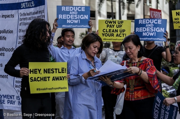 그린피스 활동가들은 네슬레 필리핀 본사 앞에서 플라스틱 사용 감축을 촉구하는 시위를 벌였다. 네슬레 필리핀 임원 크리스틴 폰체 가르시아(사진 가운데)가 활동가들의 요구 서한과 네슬레의 일회용 플라스틱 포장재의 비용을 기재한 청구서를 받아 들고 있다.