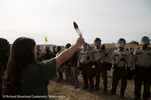다코타 송유관 건설에 대항하는 물 지킴이들(Water Protectors)이 스탠딩 락 근처 캠프에 줄지어 서있는 경찰들 앞에서 독수리 깃털을 손에 쥔 채 시위하고 있습니다.