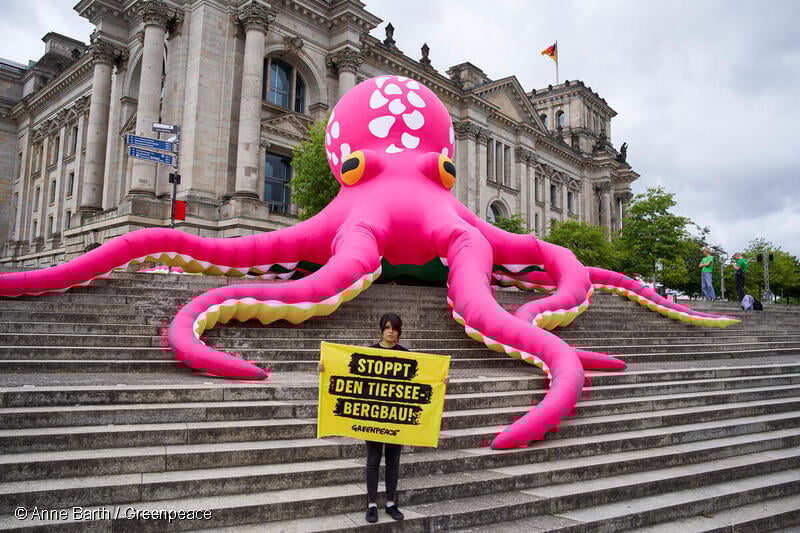 그린피스 액티비스트가 문어모양의 조형물 앞에서 배너를 들고있다.