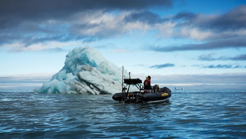 Greenpeace inflatable in front of a blue iceberg in Scoresby Sund fjord, east coast of Greenland.