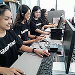 Four enthusiastic telefundraisers sitting at a call desk. They are wearing headsets and speaking into microphones while looking at computer screens.