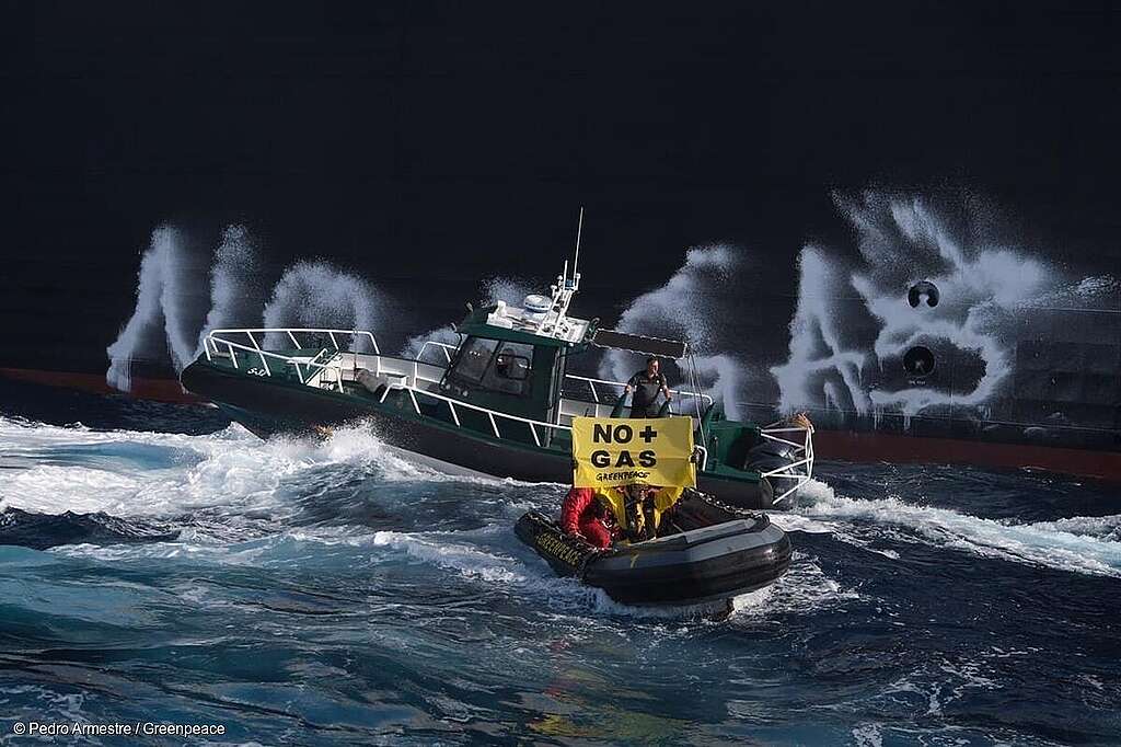 Fotografía panorámica en la que activistas de Greenpeace, a bordo de lanchas en el mar, sostienen mantas con el mensaje "NO + GAS" frente a un buque cargado con gas fósil licuado. Fotografía panorámica en la que activistas de Greenpeace, a bordo de lanchas en el mar, sostienen mantas con el mensaje "NO + GAS" frente a un buque cargado con gas fósil licuado.