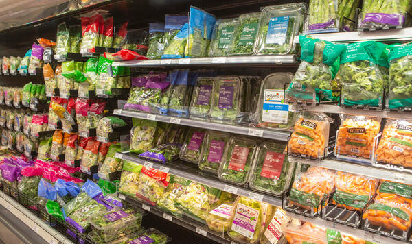 Fotograf&iacute;a de un estante de s&uacute;per mercado lleno de frutas y verduras envueltas en pl&aacute;stico.