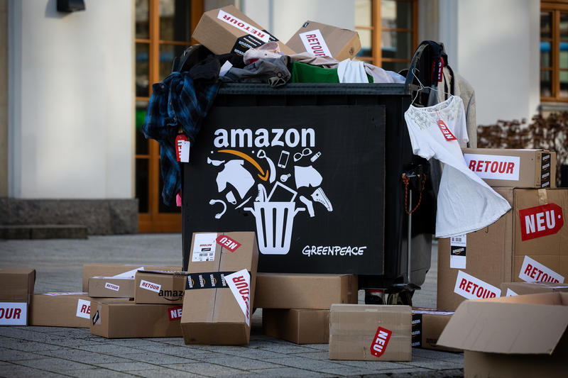 Caja de basura con el logo de Amazon y cajas de cartón simulando deshechos.