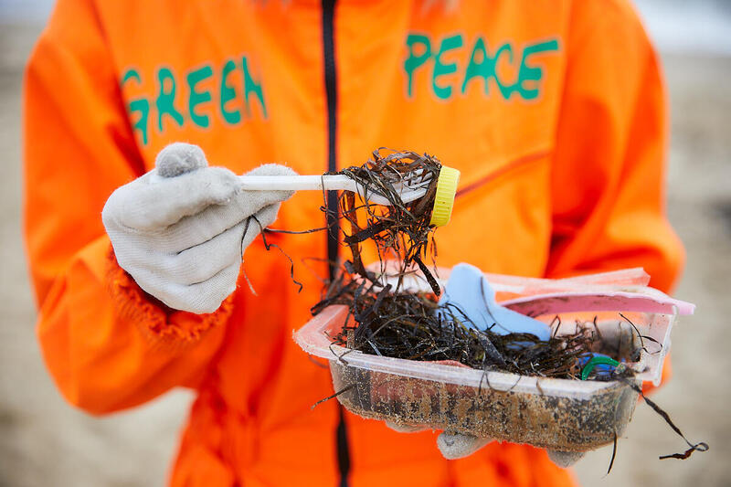 Activista de Greenpeace sosteniendo un recipiente de plástico con basura plástica.
