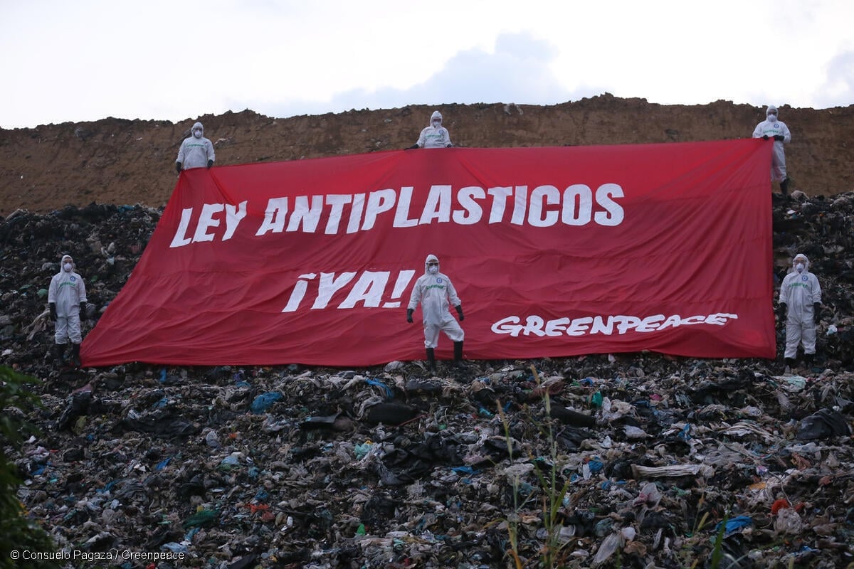 Activistas de Greenpeace México portando trajes de protección en un basurero a cielo abierto de Villa Allende, municipio de Coatzacoalcos, Veracruz, mientras sostienen un amanta en la que se lee "Ley antiplásticos ¡ya!"