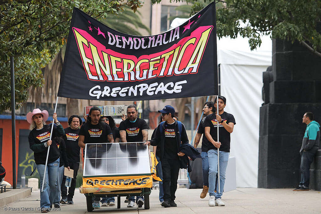 Activistas de Greenpeace México caminando por las calles de CDMX llevando un panel solar y una bandera que dice 'democracia energética', promoviendo el acceso a la energía renovable.