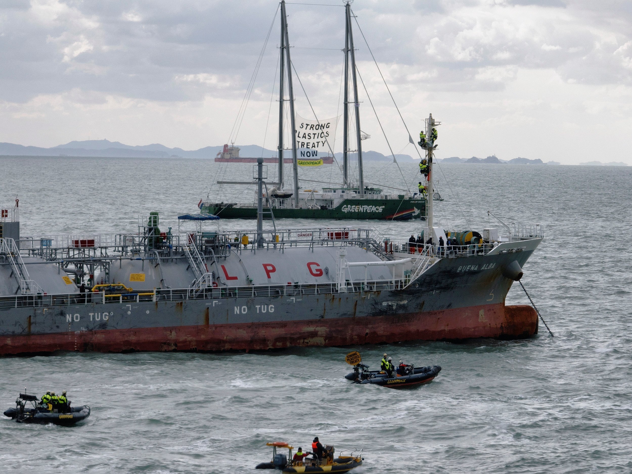 Activistas de Greenpeace en balsas rodean un barco petroquímico marcado con "LPG"; al fondo se ve un barco de Greenpeace con una bandera que dice "Strong plastics treaty now".