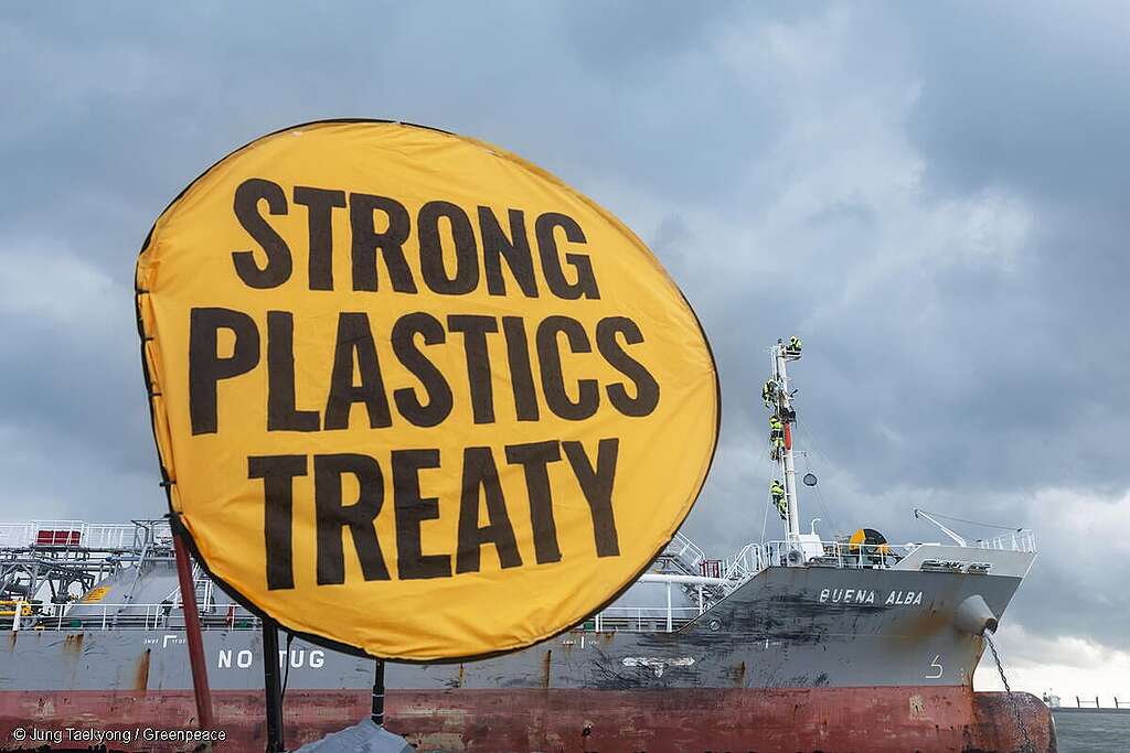 Barcos en el mar durante una protesta pacífica, con una bandera de Greenpeace que dice "Strong Plastics Treaty" en primer plano.