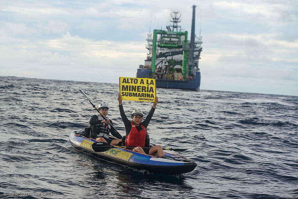 Activistas de Greenpeace México en una balsa sosteniendo el mensaje "Alto a la minería submarina", de fondo un buque de perforación de The Metals Company.