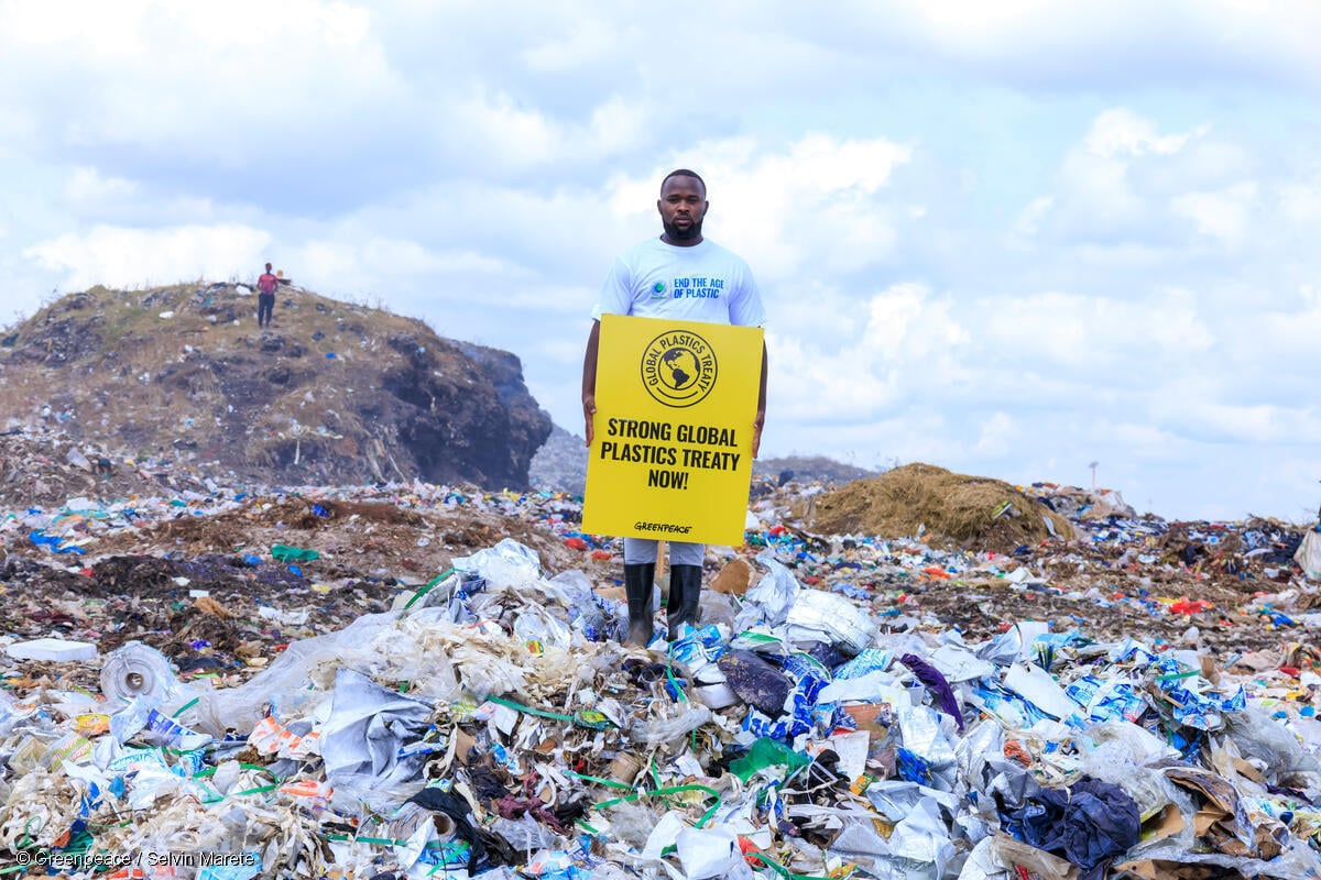 Activista en el vertedero de Dandora en Kenia sostiene el mensaje "Tratado Global de Plásticos Sólido ahora"