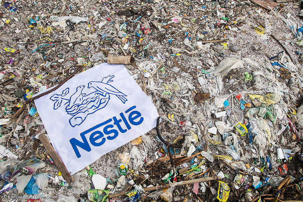 Montaña de residuos plásticos cubierta por una manta gigante con el logo de Nestlé, evidenciando el impacto ambiental de sus empaques desechables. Montaña de residuos plásticos cubierta por una manta gigante con el logo de Nestlé, evidenciando el impacto ambiental de sus empaques desechables.