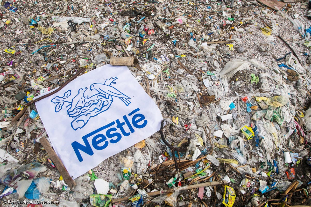 Montaña de residuos plásticos cubierta por una manta gigante con el logo de Nestlé, evidenciando el impacto ambiental de sus empaques desechables.
