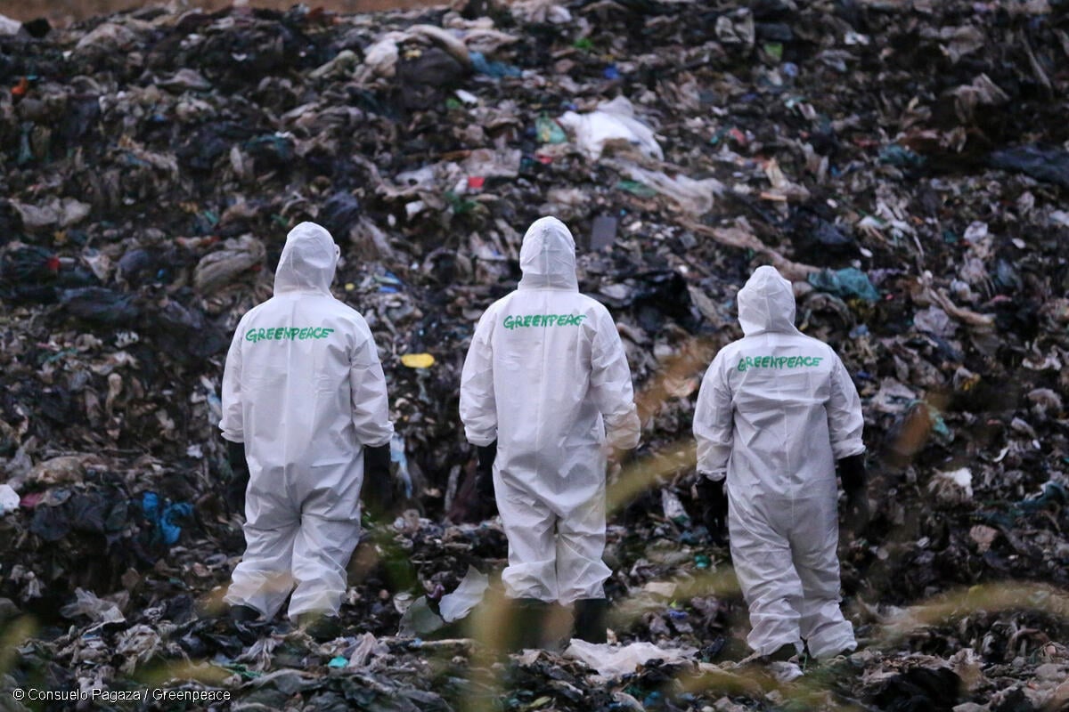 Tres activistas de Greenpeace México con trajes de protección protestan frente a un basurero para exigir una ley contra plásticos de un solo uso.