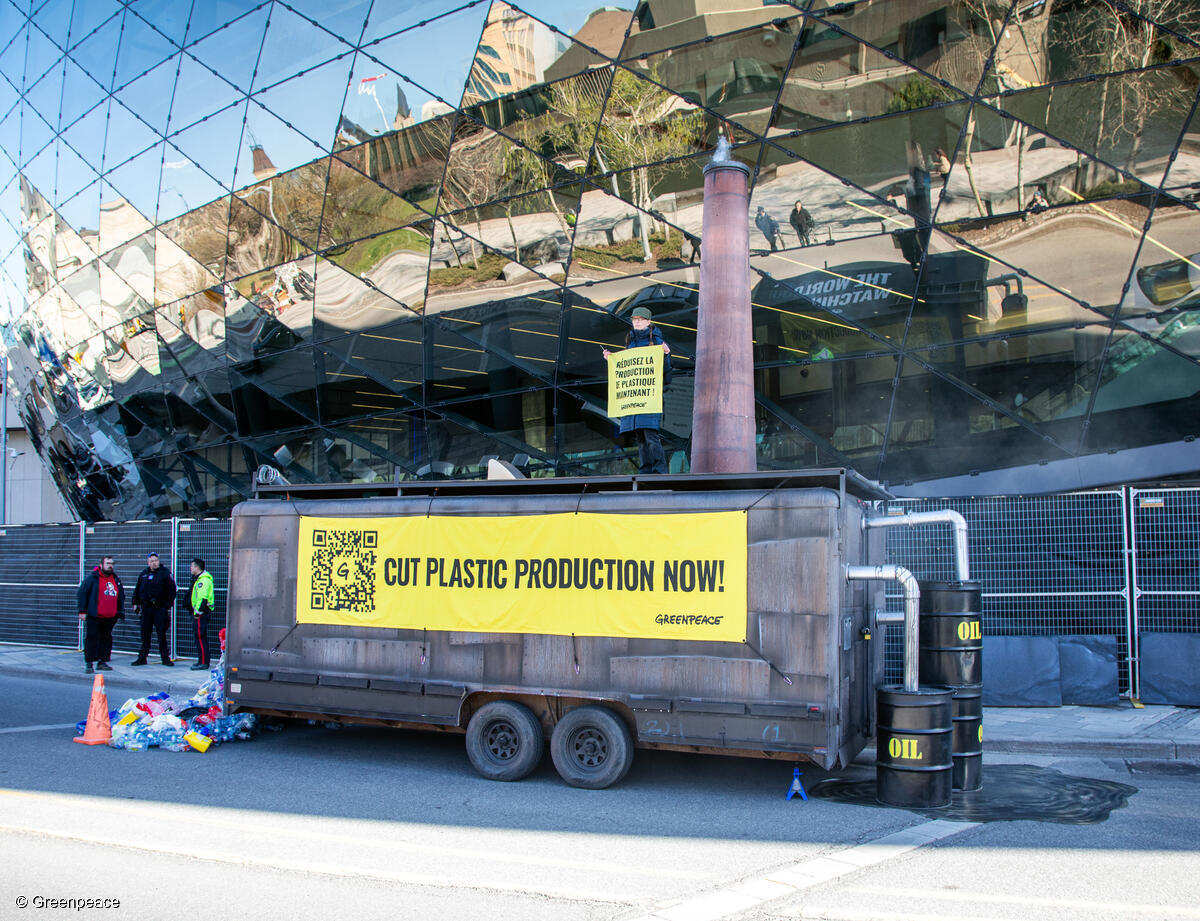 Maqueta de fábrica global de plásticos con imágenes de petróleo convertido en contaminación plástica y mensajes que como: "¡Reduzcan la producción de plástico ya!"