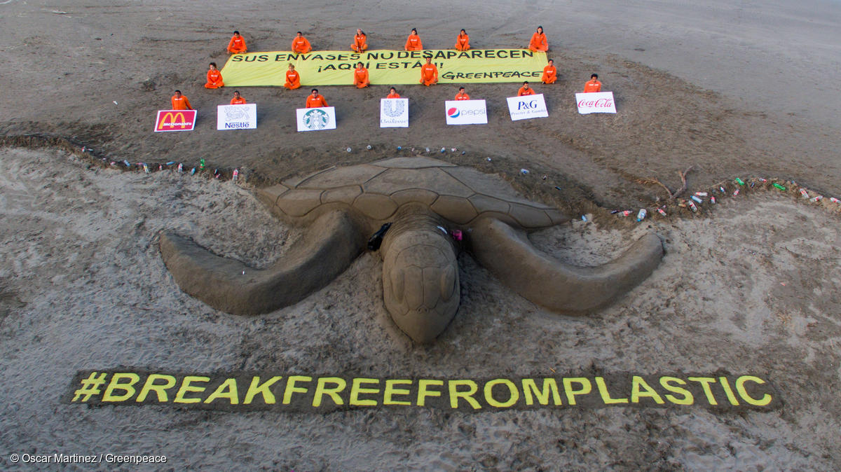 Activistas de Greenpeace México crean una gran escultura de arena de tortuga marina para resaltar el problema de la contaminación plástica, mientras sostienen una manta que dice "Sus envases no desaparecen. Aquí están"